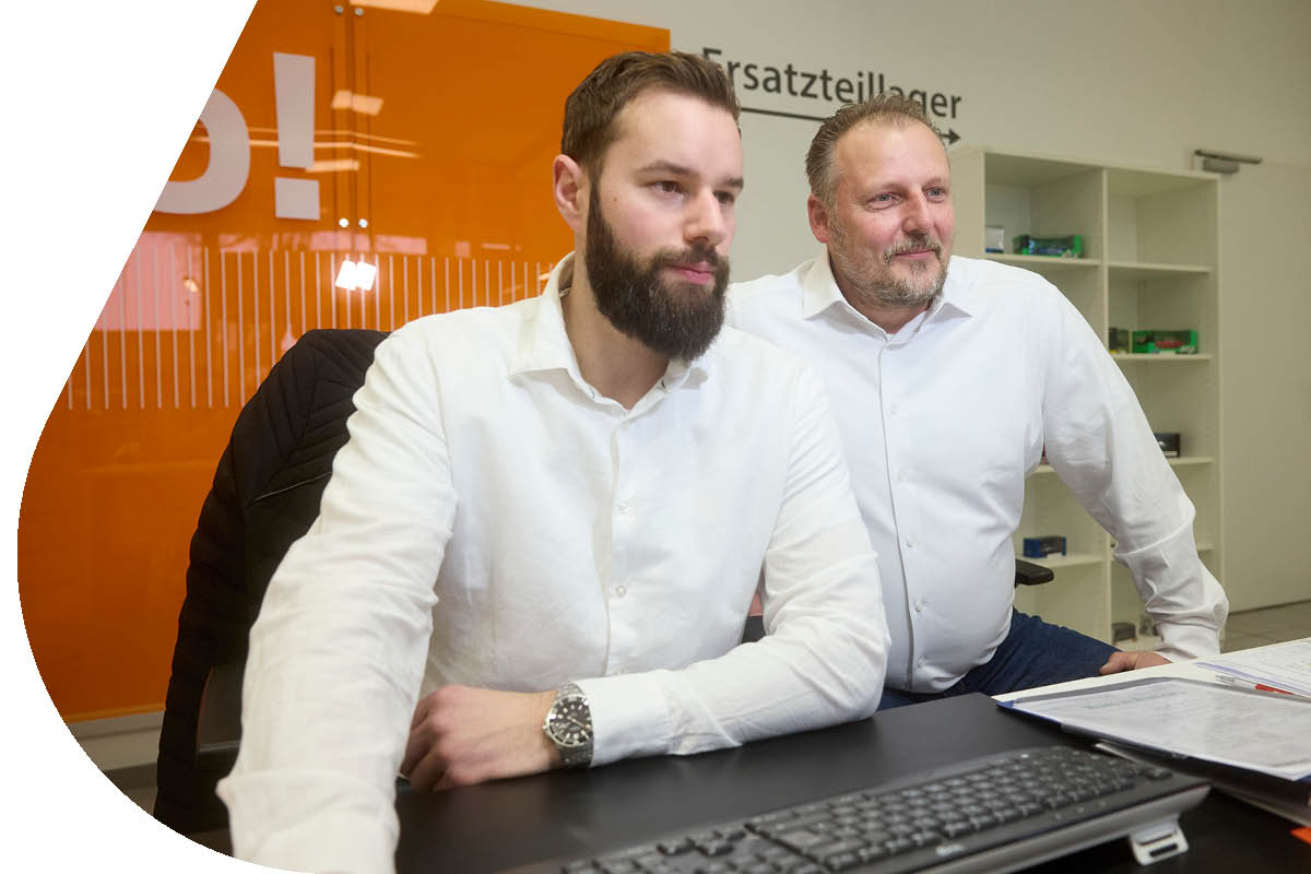 Zwei Mitarbeiter sitzen am Schreibtisch und schauen auf einen Bildschirm